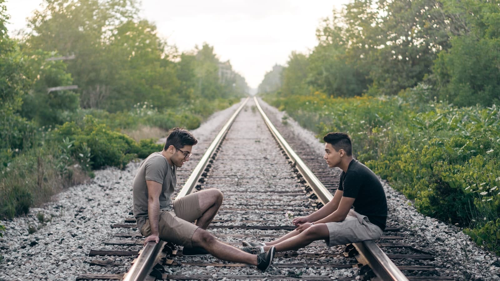 Two people sitting on railroad tracks facing each other