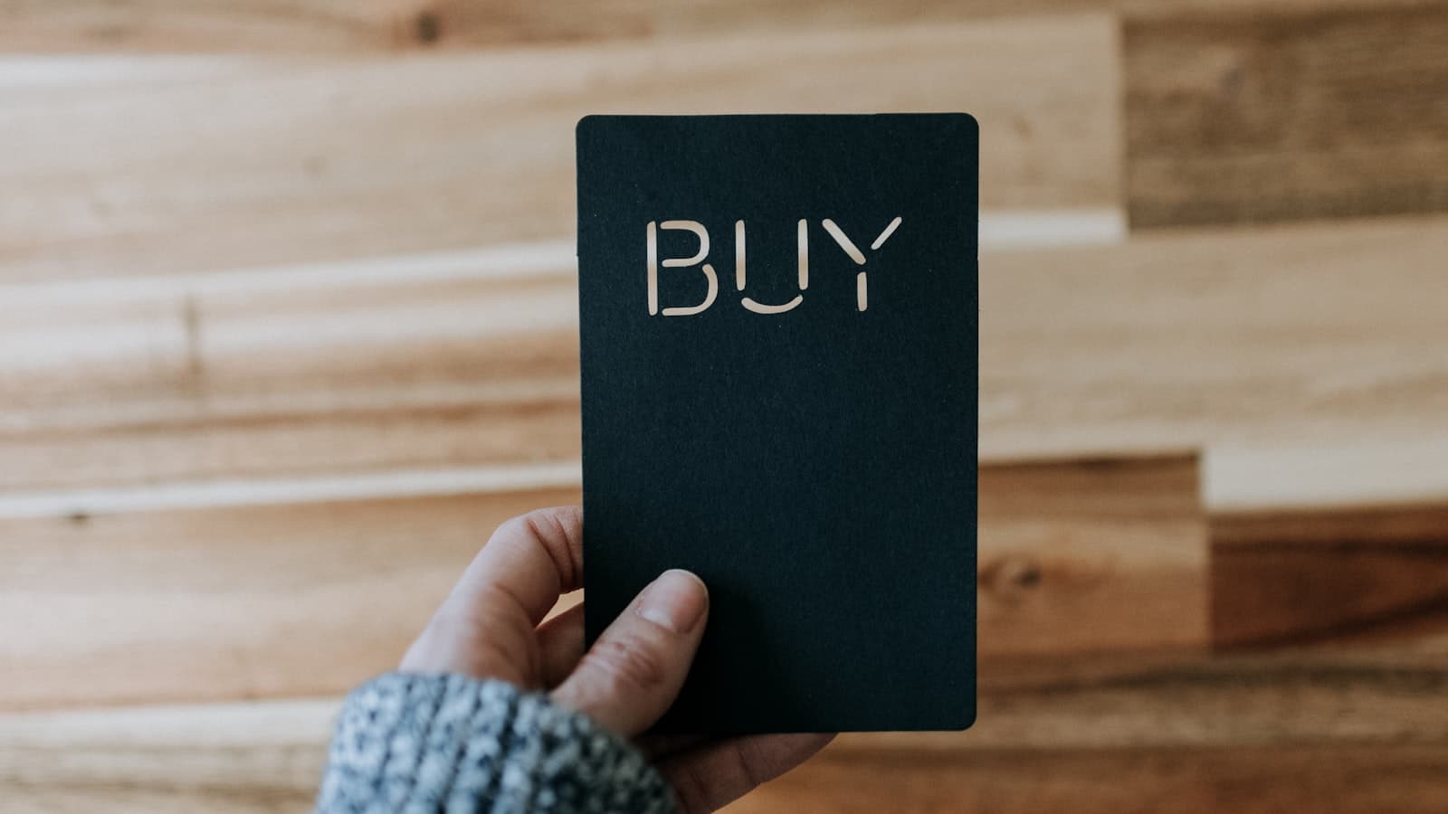 A hand holding a black card that says BUY