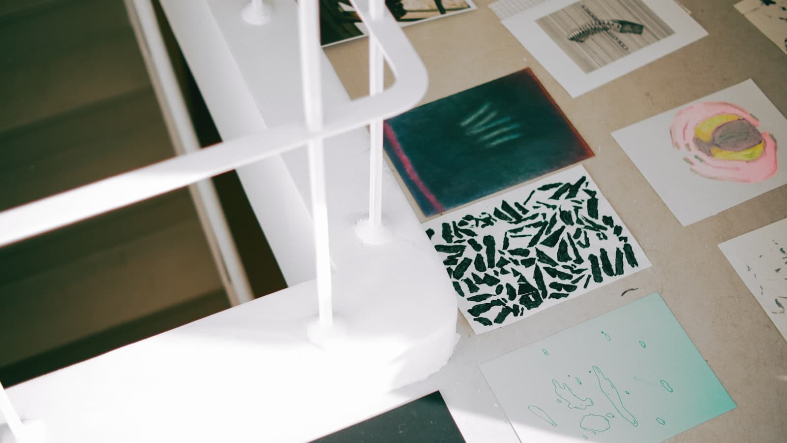 Art cards and sketches spread across a tabletop with a white chair in the foreground